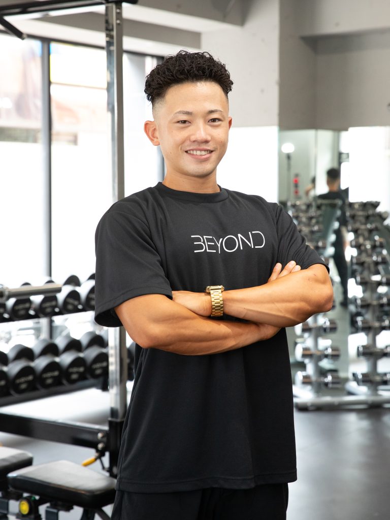 BEYOND武蔵小杉のパーソナルトレーナー吉田がジム内で笑顔で腕を組んでいる写真