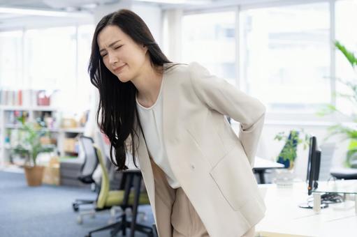 オフィスで腰に手を当て痛みを感じる女性