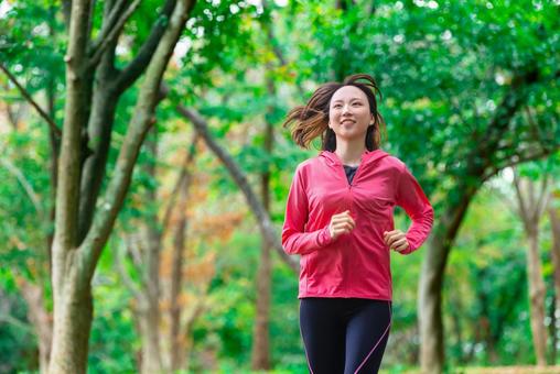 秋模様の公園でランニングをする女性。運動に適した気候と季節感を表現。