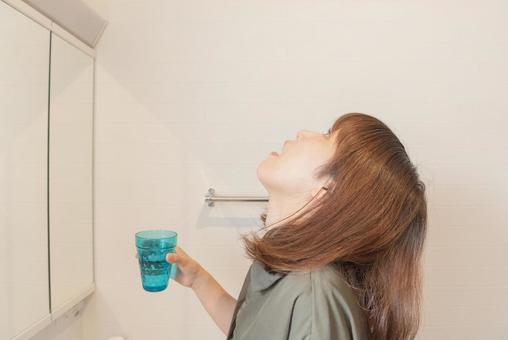 コップを持ち、うがいをしている女性。風邪予防の基本的な行動を表現。