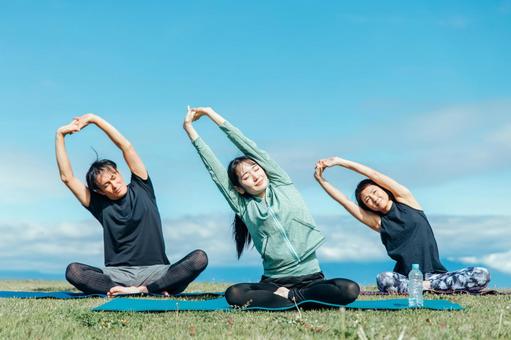 屋外でストレッチをする男女3人。太陽の下で体を温める様子。