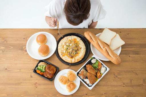 パンやピザなどの高カロリー食品を前に食べ過ぎてしまう女性の写真。秋の食欲暴走を象徴。
