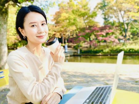 公園でコーヒーを飲みながらリラックスする女性(秋の屋外)