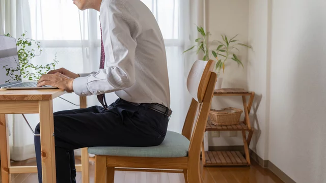 猫背姿勢でパソコン作業中に肩こりや首こりを感じている人物
