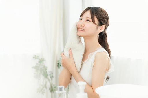 朝に洗顔後タオルで顔を拭く女性。清潔で明るい印象