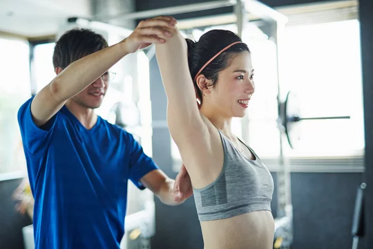 トレーナーが女性の肩の位置を整えながら姿勢改善をサポートしている様子
