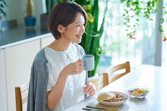 「朝食をとりながら温かい飲み物を飲む女性」