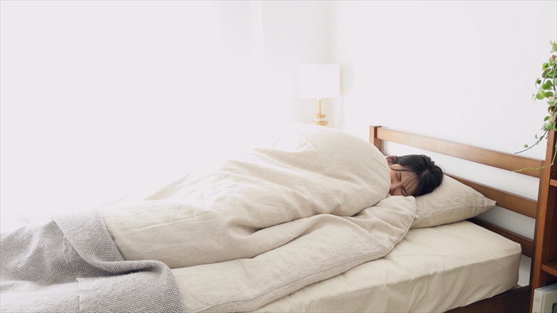 「冬の朝に寒さで布団にくるまって起きられない女性」