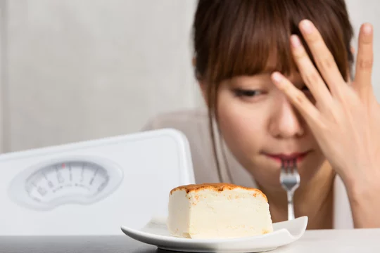 ケーキを前に食べるか迷う女性。無理な食事制限をせずにダイエットを成功させる方法を表すイメージ。
