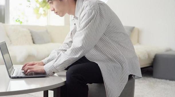 前かがみの姿勢でノートパソコン作業をしている男性