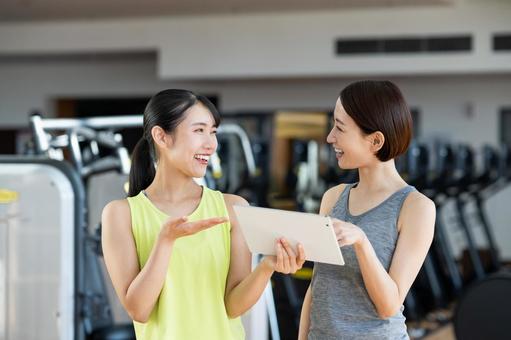 ジムでトレーナーと体調や運動について相談している女性