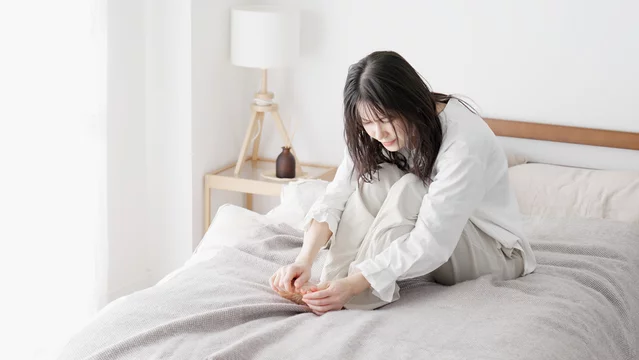 冬の朝にだるさを感じてベッドに座っている女性